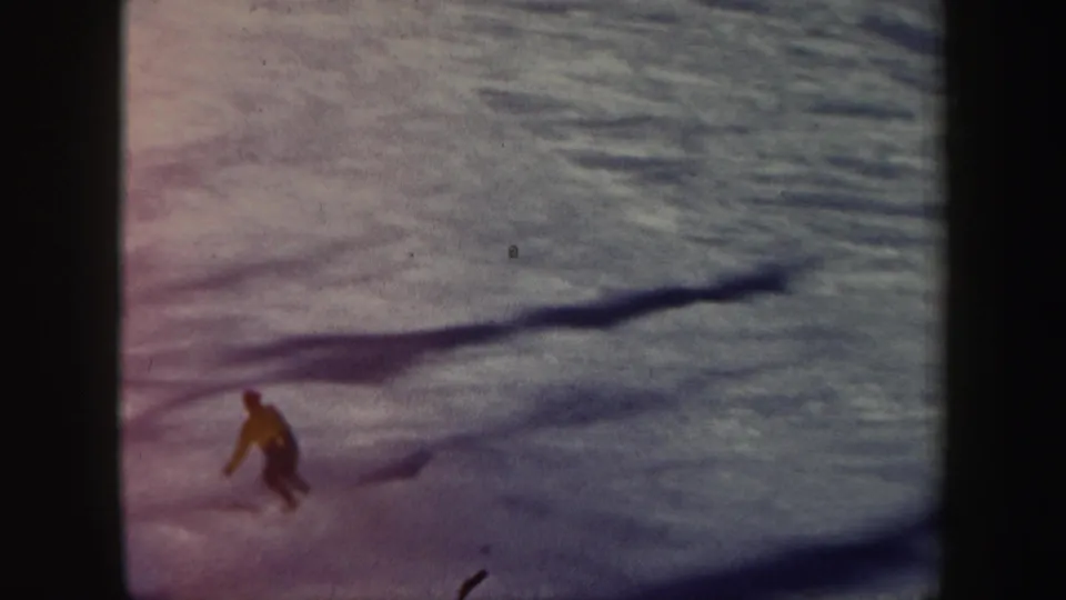 The yellow-jacketed skier crosses the Vermont slope in soft 8mm focus, with dark shadows stretching over the snow.