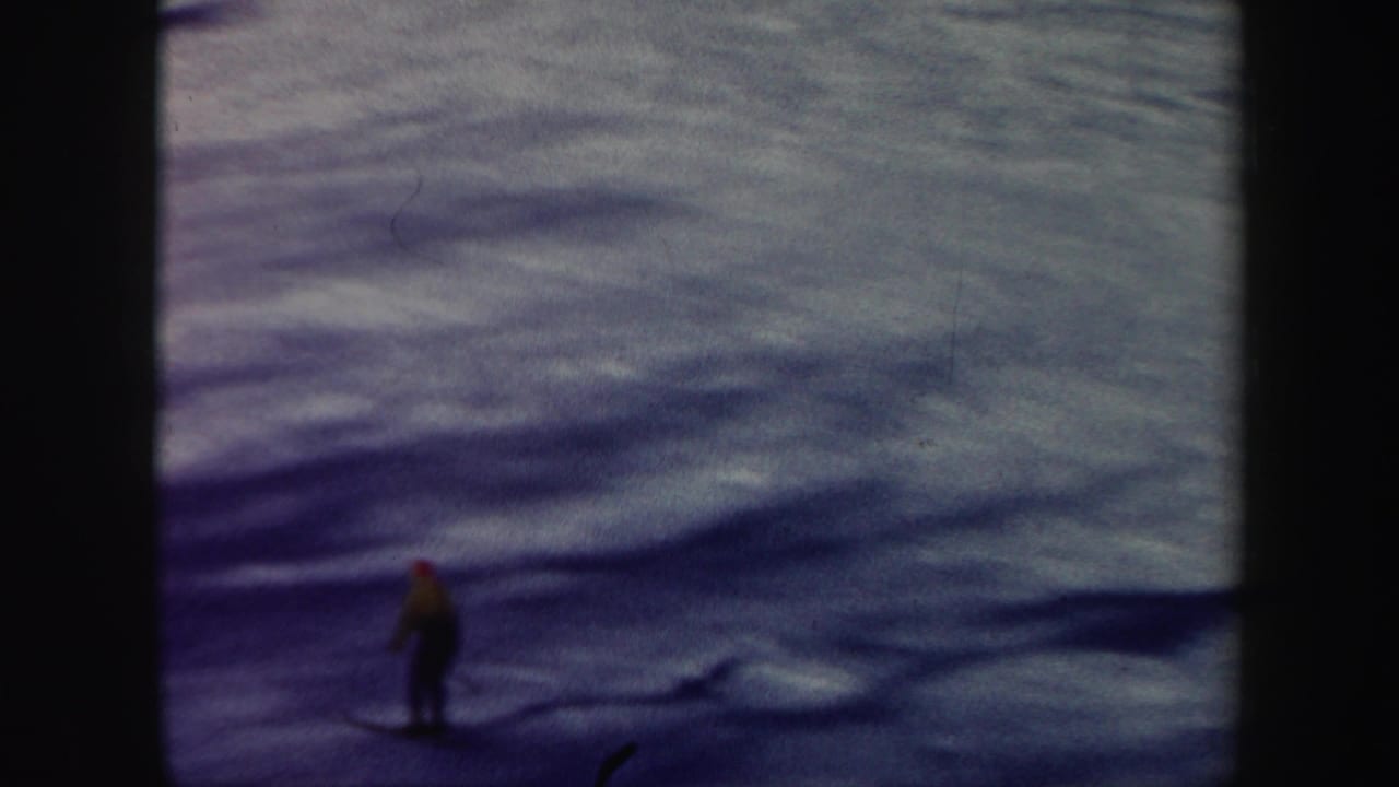 Distant skier in a yellow jacket descending a snowy slope under a pale sky.