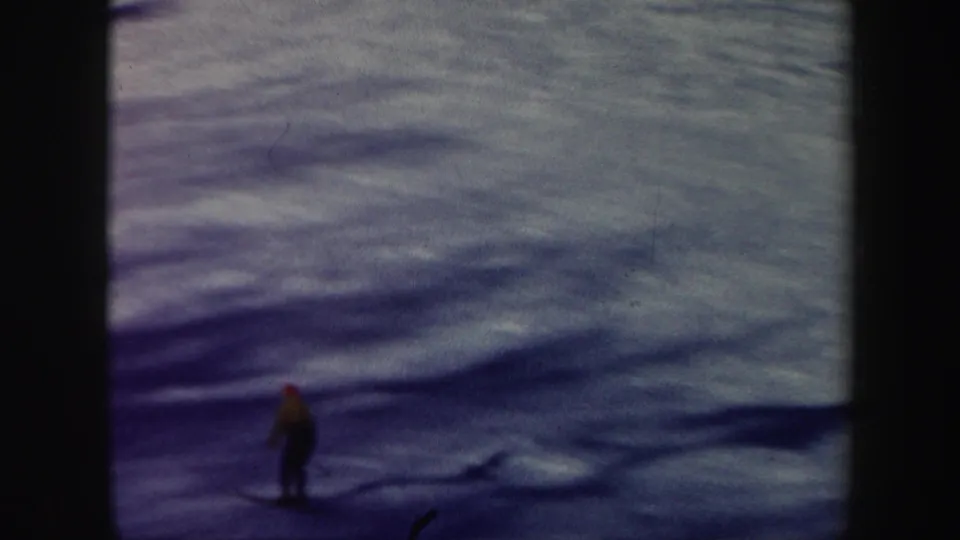 A distant skier in a yellow jacket moves across a snow-covered Vermont slope in 1962 home-movie footage.