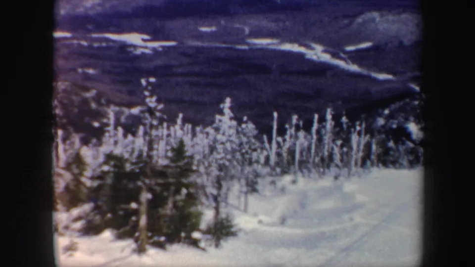 1962 Vermont 8mm frame with snow-covered trees in the foreground and dark mountain terrain beyond.