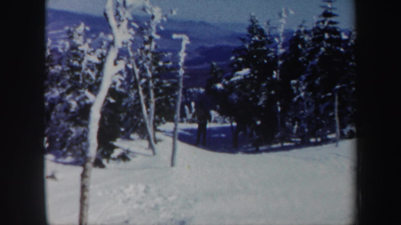 1962 Vermont 8mm frame showing a distant skier on a snow-covered run between frosted trees, with blue mountain ridges in the background.