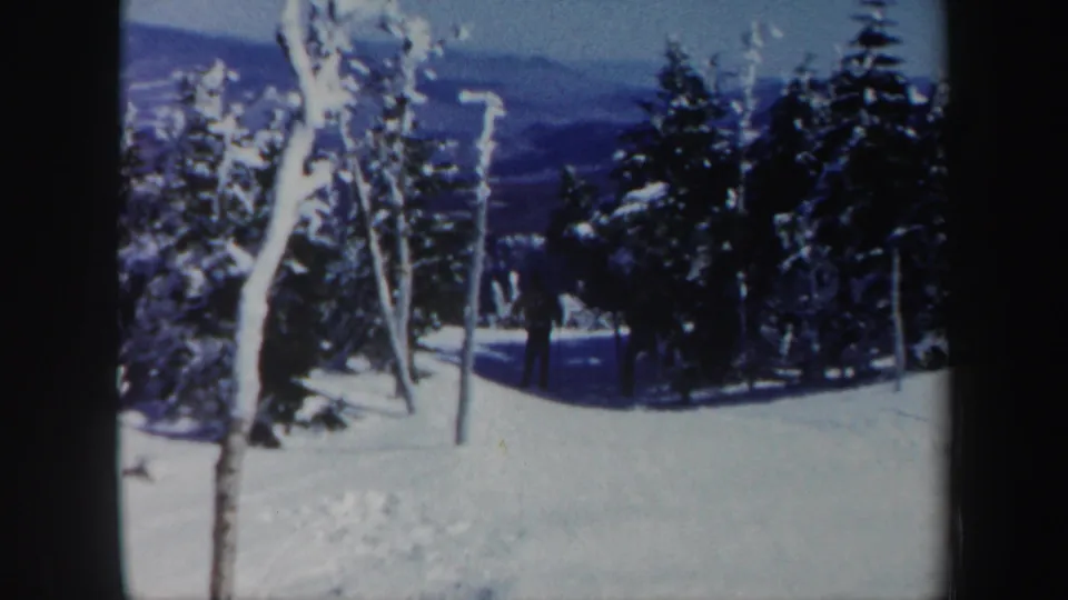 1962 Vermont 8mm frame showing a distant skier on a snow-covered run between frosted trees, with blue mountain ridges in the background.