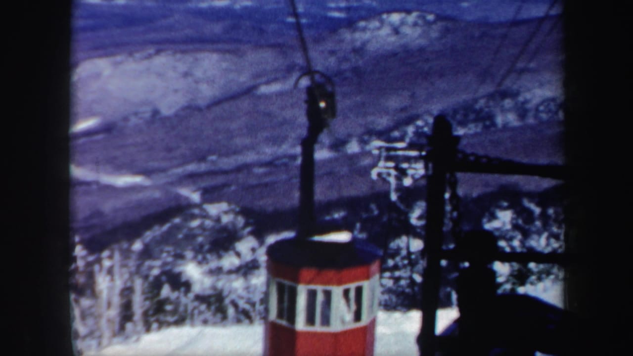 Red cable car on overhead cables above a snowy mountain landscape.