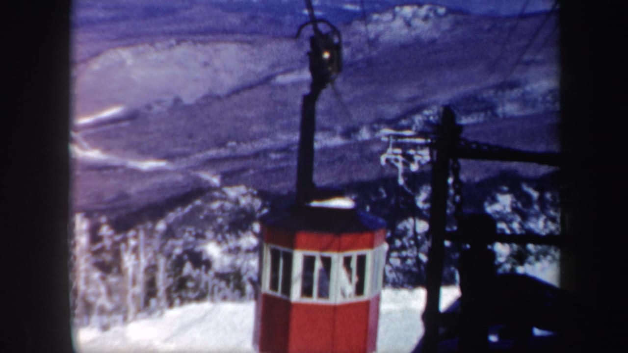 The red cable car appears beside lift equipment, with blue-toned snowy terrain and wooded slopes in the background.