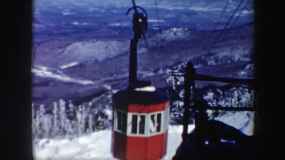 The red cable car sits partly low in frame as overhead cables stretch across a snowy Vermont mountain landscape.