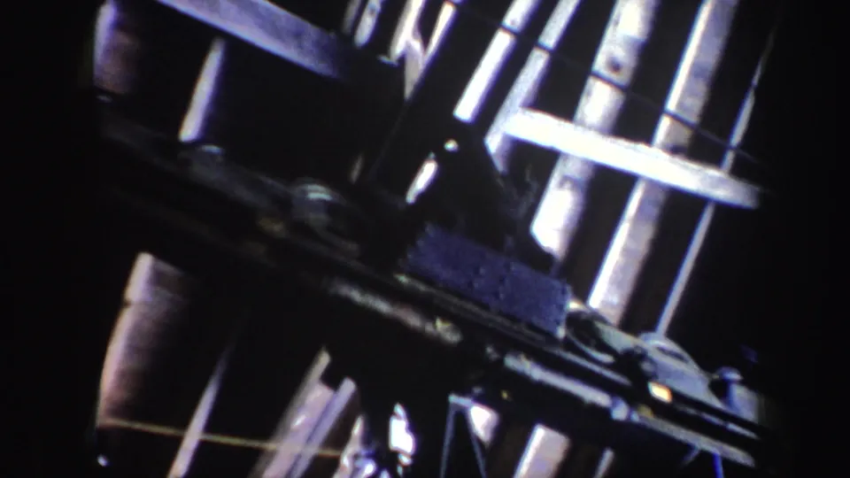 1962 Vermont home-movie frame showing close ski lift hardware, metal bars, rails, and deep shadow.