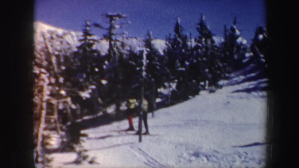 Distant figures continue ski walking through a snowy Vermont forest scene, with mountains and blue sky in the background.