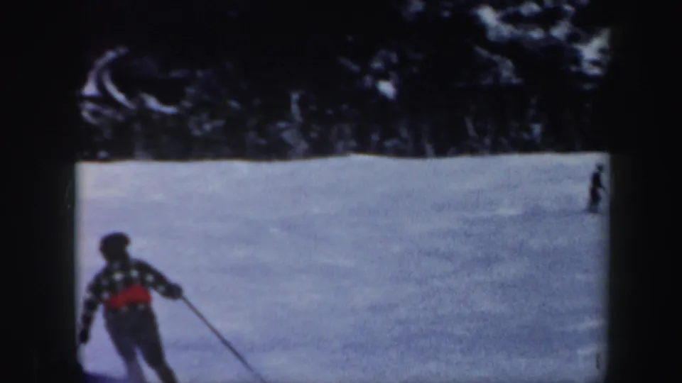 1962 Vermont 8mm frame showing a distant skier in dark outerwear with a red accent moving down a broad snowy slope.