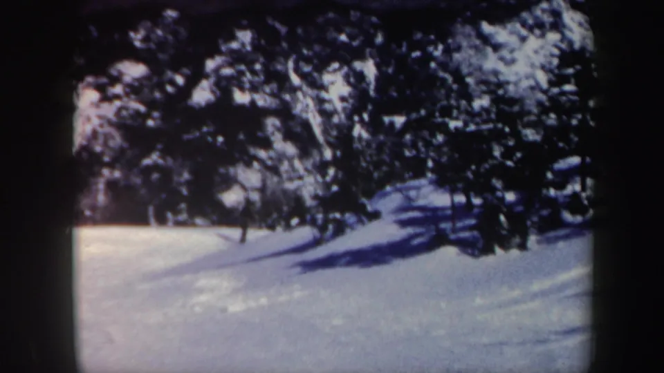 1962 Vermont home-movie frame with a distant skier near the treeline and long shadows across the snow.