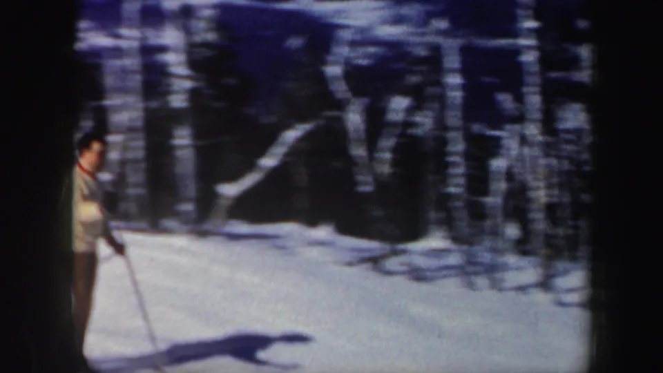 Adult man in a light sweater stands on skis near trees on a snowy Vermont slope in 1962 home-movie footage.