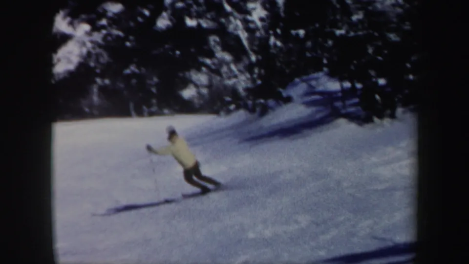 Adult skier leans into a downhill turn on a snowy wooded Vermont slope in 1962 8mm home-movie footage.