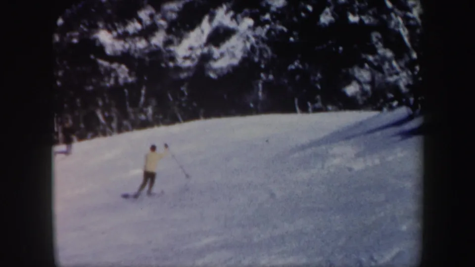Distant adult skier crosses a wide snowy Vermont slope with a dark forested hillside behind him.