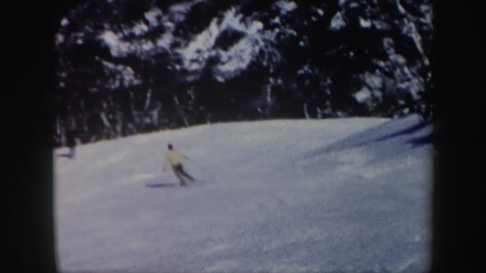 1962 Vermont 8mm frame showing a skier in a light top moving across a snowy slope near evergreen trees.