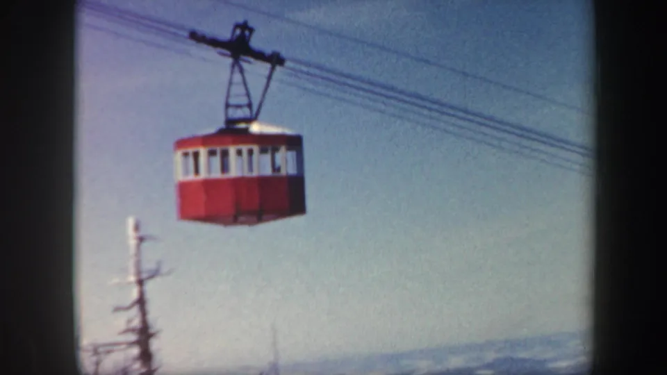 Red cable car suspended on wires above a snowy landscape in 1962 Vermont resort footage.