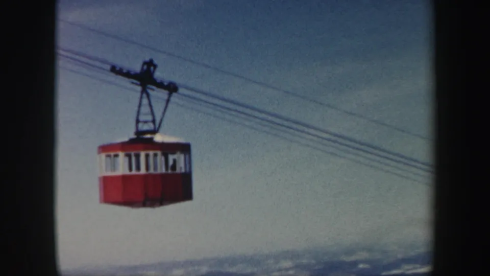 1962 Vermont 8mm frame of a red cable car moving along wires above a winter landscape.