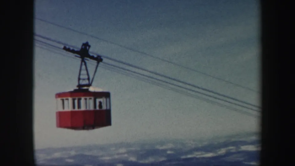1962 Vermont 8mm frame showing a red gondola car on overhead cables above a snow-dusted mountain landscape.