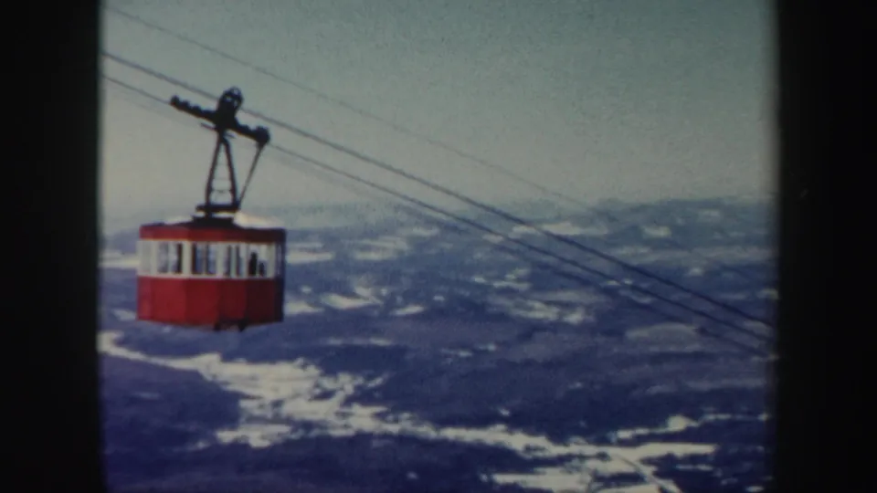 A red Vermont gondola cabin rides along cables above wooded hills and scattered snow in a 1962 home-movie frame.