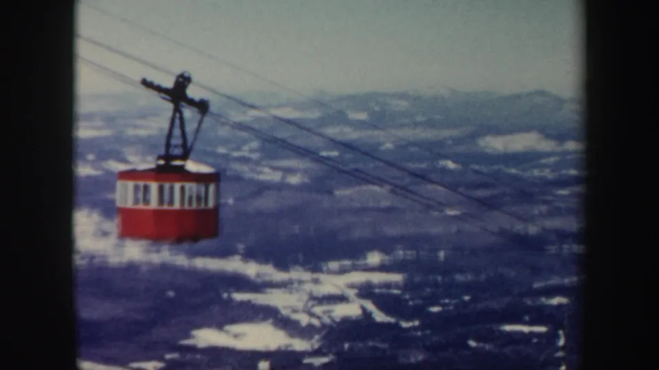 Late-frame view of the red gondola suspended over Vermont mountain ridges with scattered snow and faded 8mm color.
