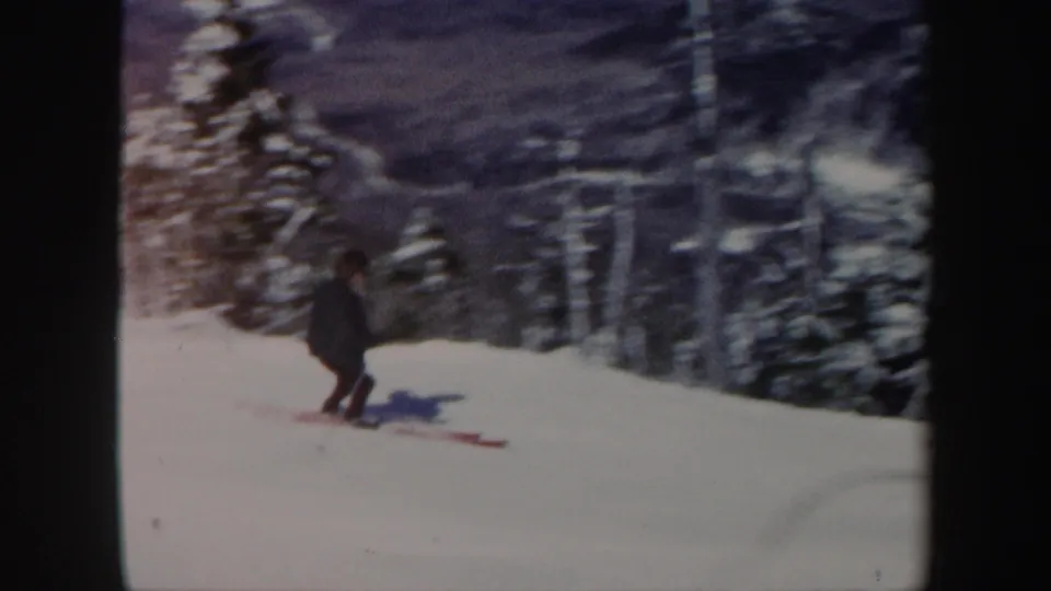 A woman skis downhill on a snowy Vermont slope, seen at a distance against dark evergreen trees.