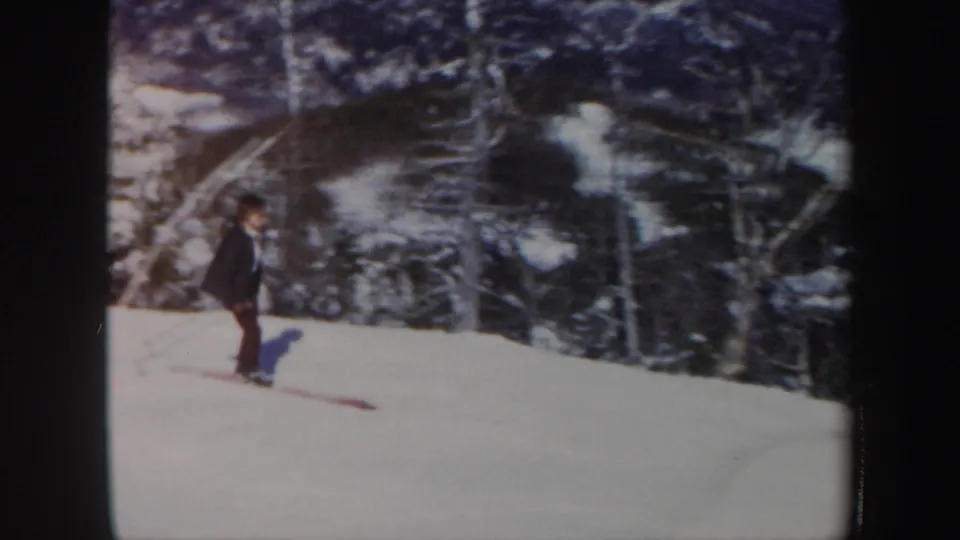 A woman skier crosses the open snow in Vermont, framed by dense winter evergreens and soft 8mm color.