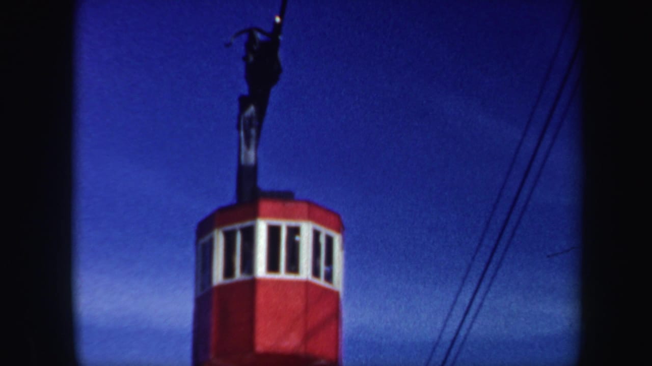 1962 Vermont home-movie still showing the red ski-lift cabin higher in frame with white windows and cable lines at right.