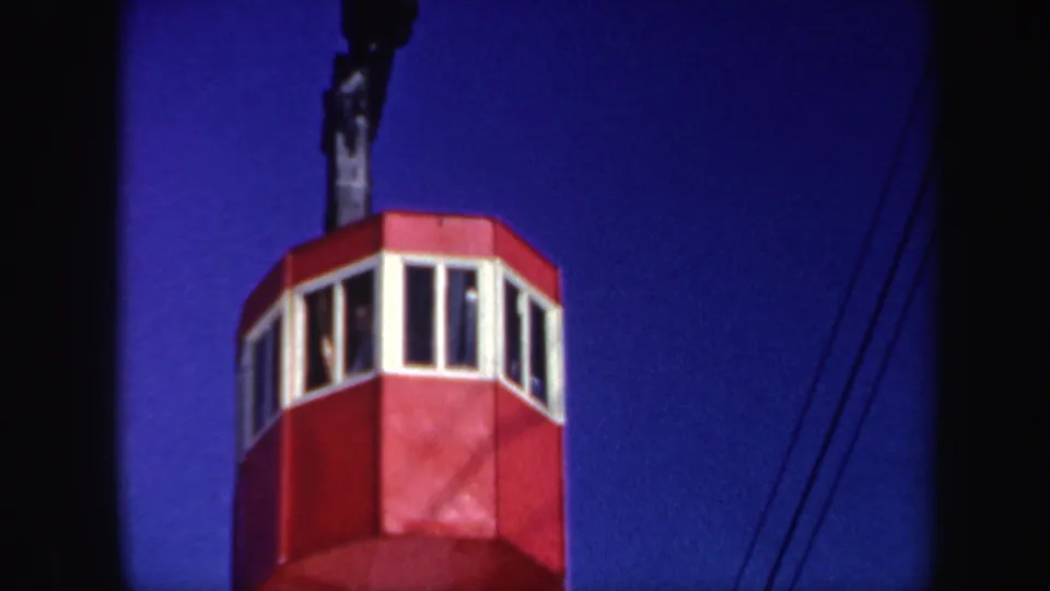 1962 Vermont 8mm frame of the red ski-lift cabin close up, with indistinct occupants or reflections visible through the windows.