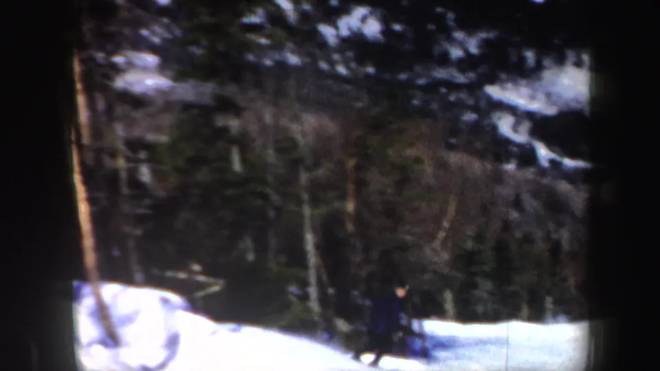 A small skier figure travels across a snowy slope below wooded Vermont hills in archival 1962 home-movie footage.