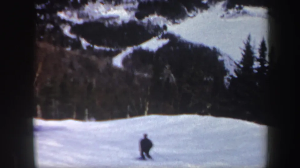 Distant skier crosses an open snowy area with a wooded mountain backdrop in Vermont 1962 8mm footage.