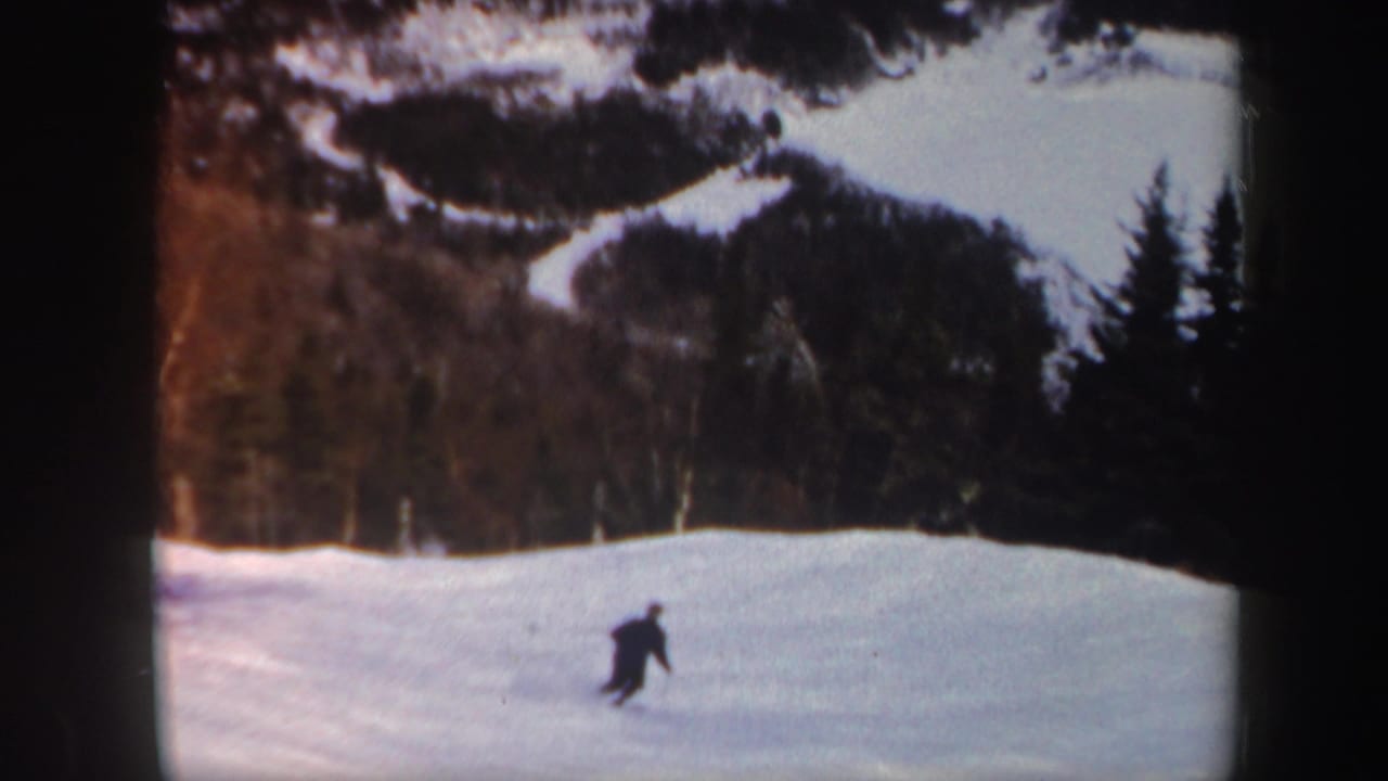 A lone skier moves across a snowy Vermont slope in 1962 home-movie footage, with forested hills behind.