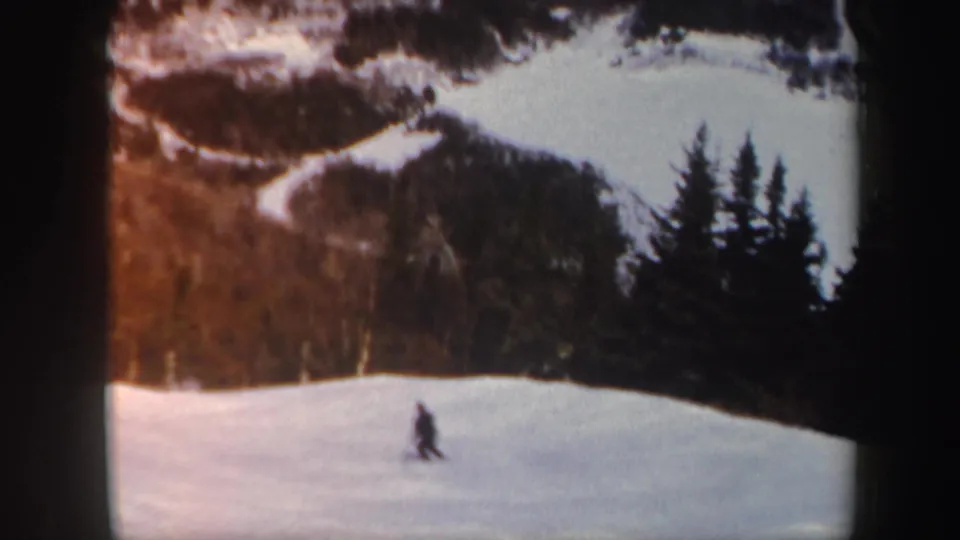 The skier appears farther across the Vermont snow slope, framed by dark trees and warm 8mm color.