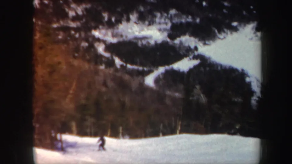 A distant skier passes near the edge of the frame on a Vermont ski slope, with snowy ground and trees visible.