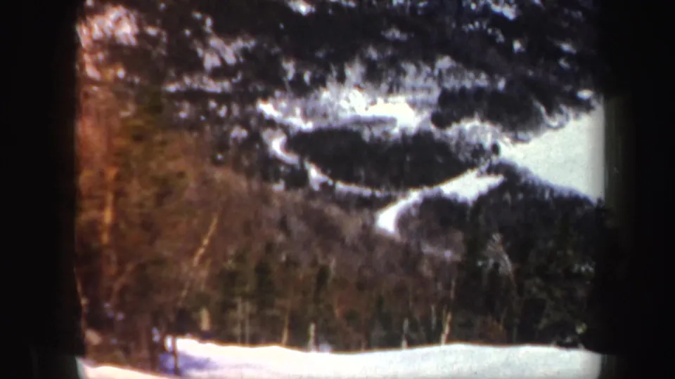 1962 Vermont 8mm frame showing snow in the foreground, a wooded mountain slope, and a distant figure near the tree line.