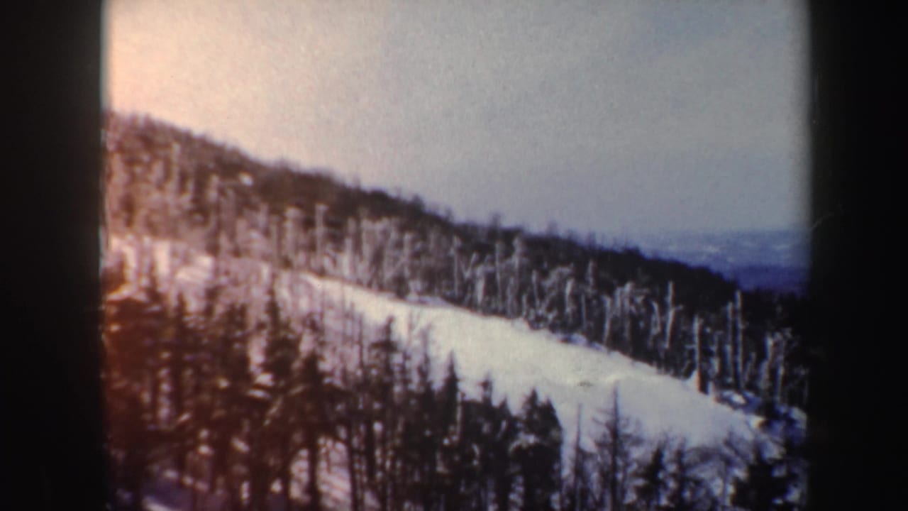 1962 Vermont 8mm frame of a snow-covered hillside and tree line with warm faded color and soft focus.