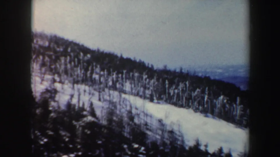 1962 Vermont 8mm frame showing a snow-covered forested ridge with a distant hazy valley beyond.