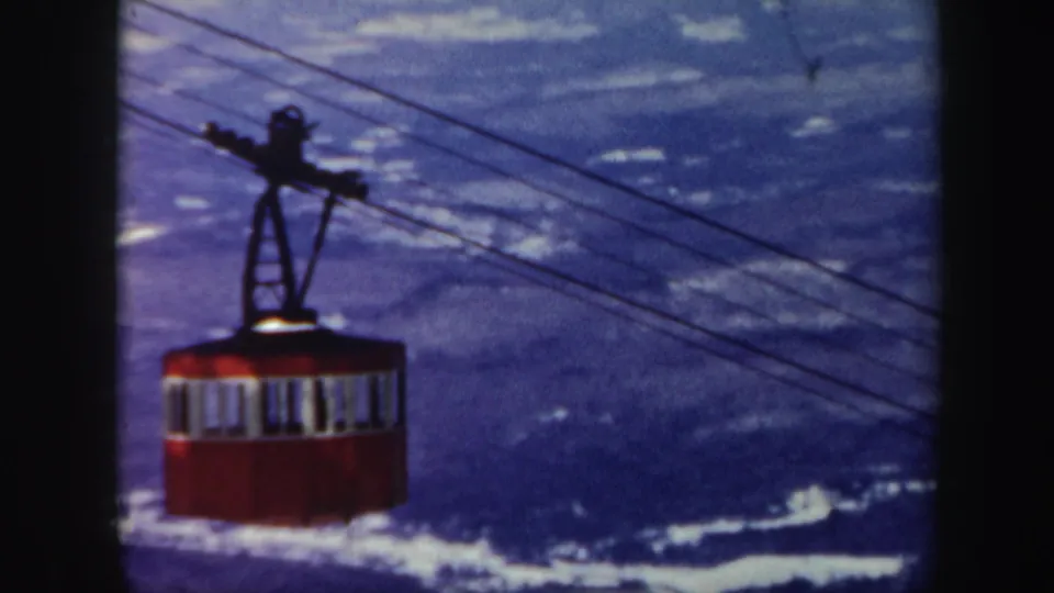 A red ski lift gondola crosses cables in front of a snowy Vermont mountain view in 1962 home-movie footage.