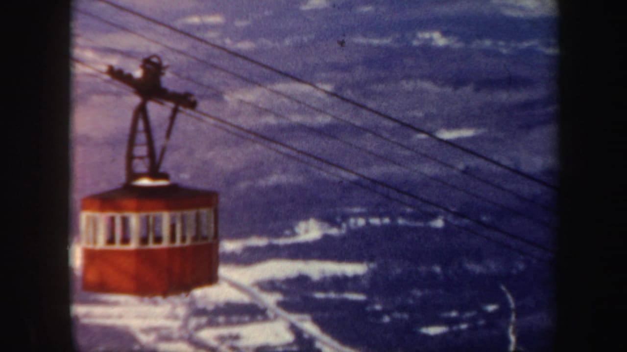 A red cable car rides along overhead wires above snowy Vermont mountain terrain in 1962 home-movie footage.