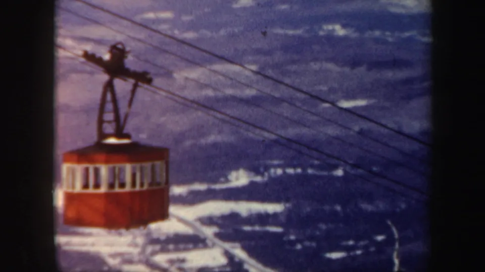 A red cable car rides along overhead wires above snowy Vermont mountain terrain in 1962 home-movie footage.