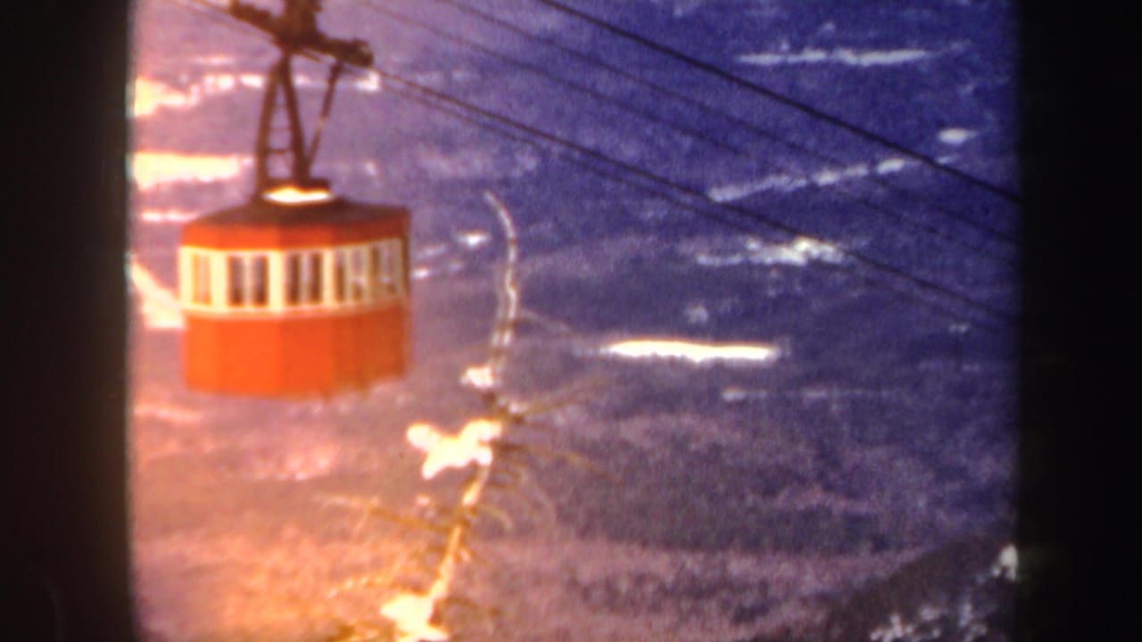 Red cable car near overhead cables with icy mountain terrain below.