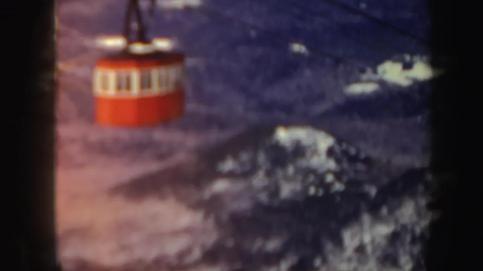 A slightly blurred red cable car passes over a snowy wooded valley in Vermont, with soft 8mm color and winter haze.