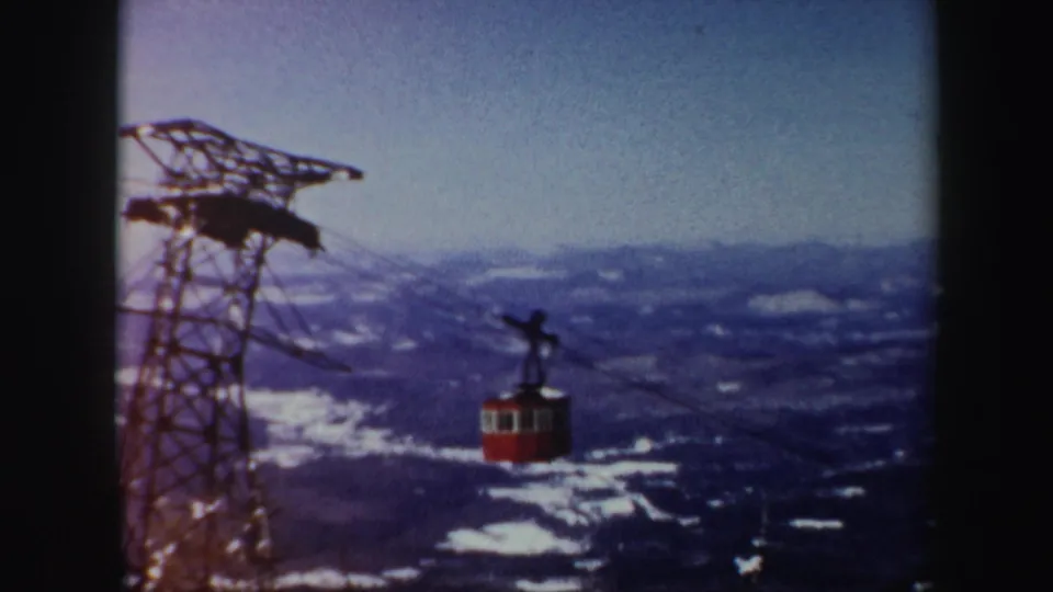 A steel tramway tower and red cable car appear against a broad snowy Vermont mountain landscape in 1962 footage.