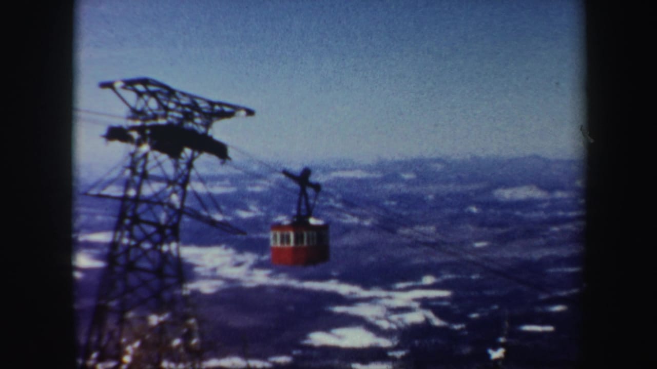 Red cable car approaches a steel tower above a snowy mountain valley.