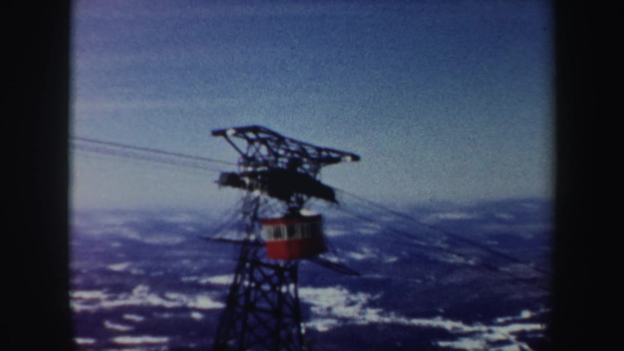Red cable car and metal tower seen against snowy Vermont mountain ridges in soft 1962 8mm color.