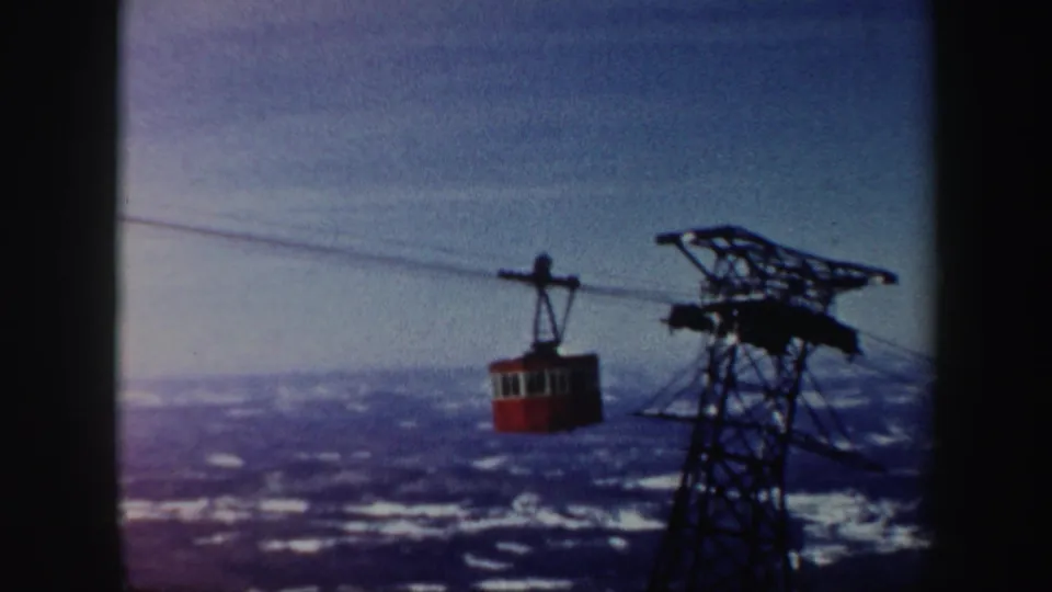 A red cable car glides along overhead cables near a steel tower over a snowy Vermont valley in 1962 home-movie footage.