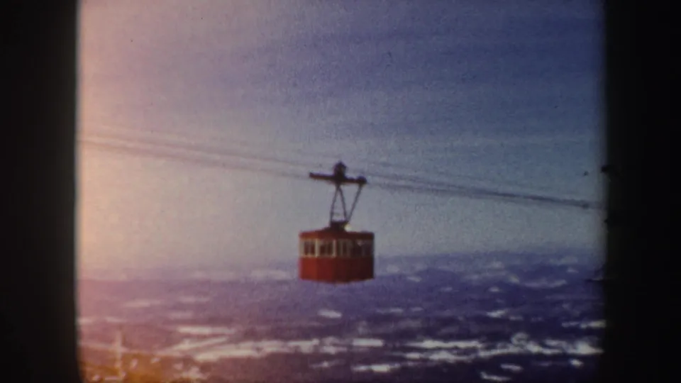 Red cable car suspended over a snow-dusted Vermont mountain valley, with faded 8mm color and soft sky exposure.