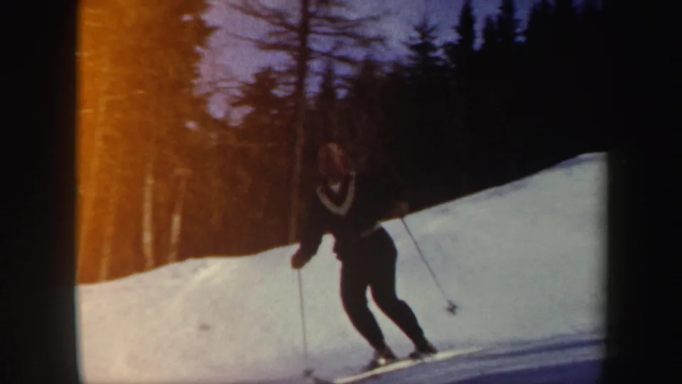 1962 Vermont home-movie frame showing a middle-aged man skiing near evergreen trees on a snowy slope.