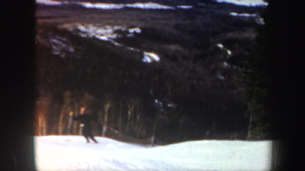 The skier continues downhill across a white slope, filmed from a distance against Vermont woods and ridges in the 1962 8mm clip.