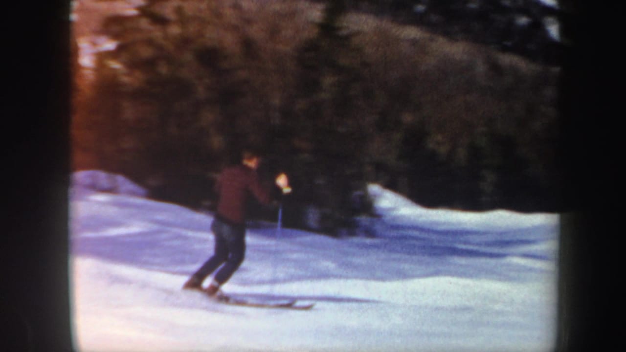 1962 Vermont 8mm frame of a skier in dark winter clothing moving across a snow-covered slope near evergreen trees.