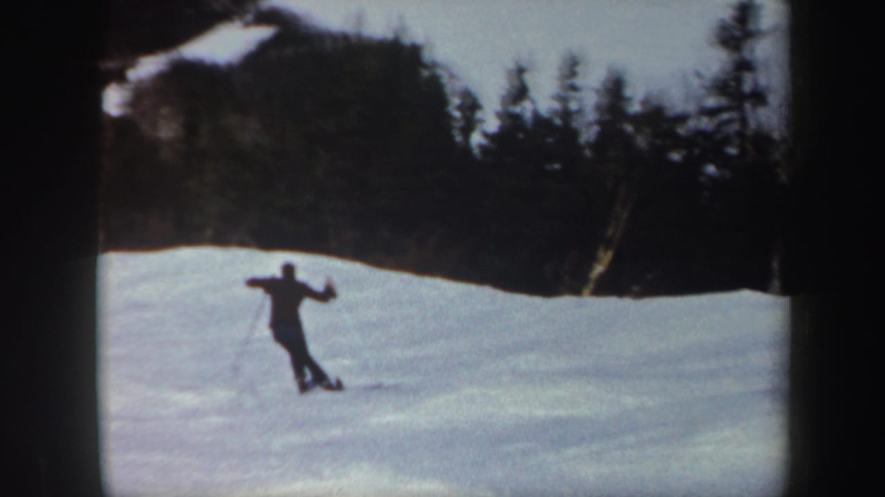 Small skier crosses an open snow slope below dark trees.