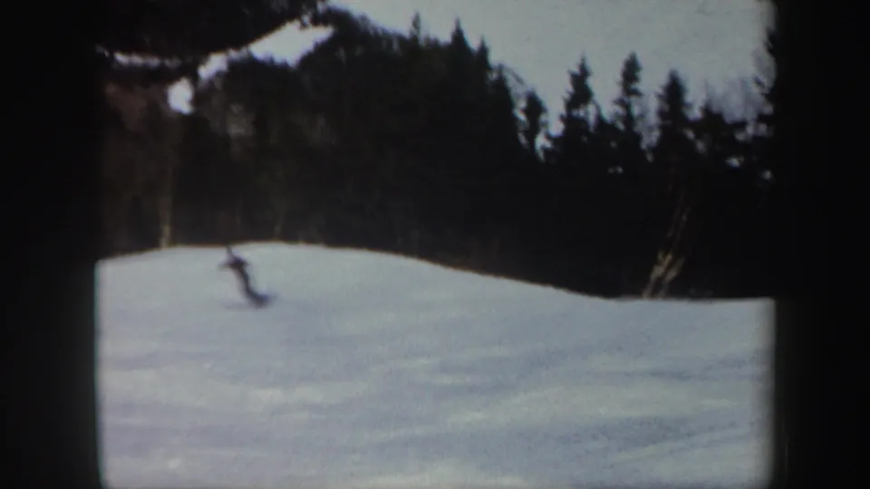 A blurred 8mm frame shows the skier farther down the Vermont snow slope, with dark trees lining the upper edge.