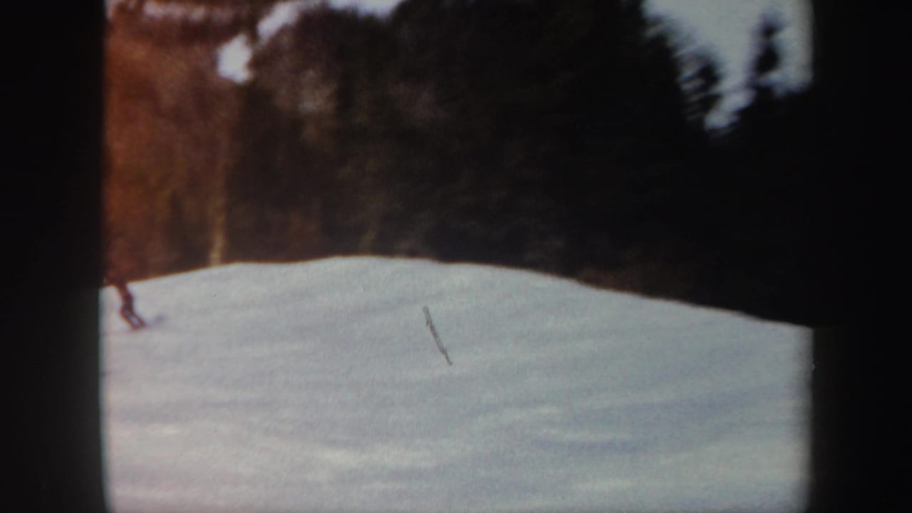 1962 Vermont 8mm frame showing a lone distant skier on a snow-covered slope bordered by winter woods.